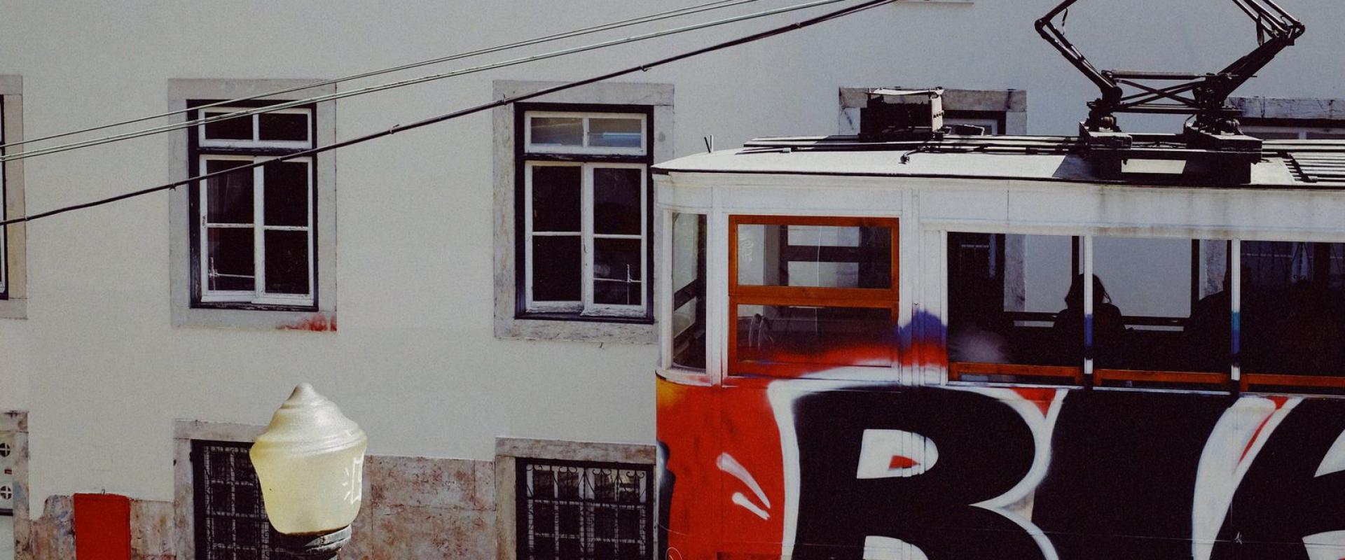 A vibrant tram adorned with graffiti travels through Lisbon, Portugal on a sunny day.