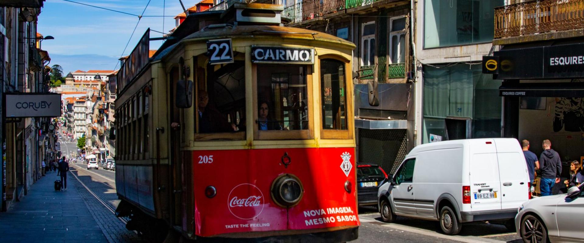 Colorful historic tram on bustling Carmo Street in Porto, showcasing urban life.