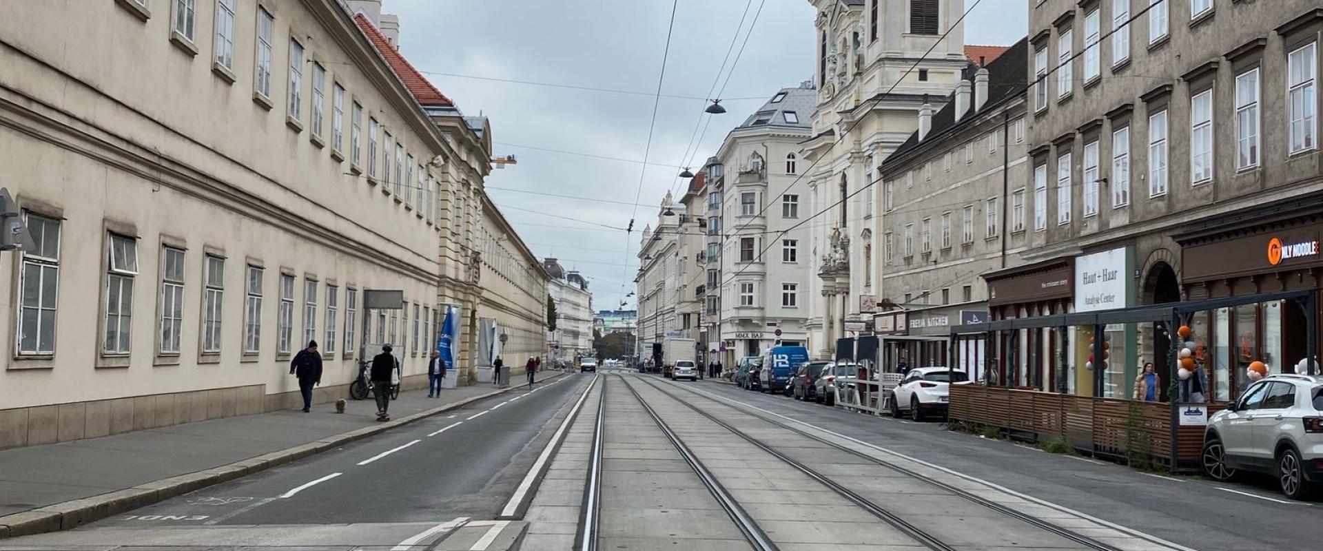 Wide-angle view of an empty city street with tram tracks leading to a historic church on a cloudy day.