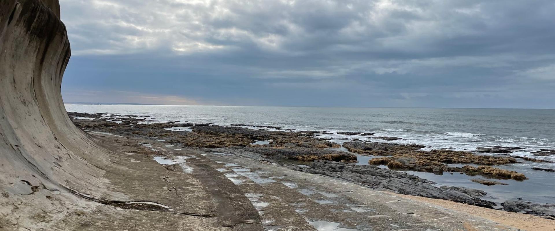 Scenic view of a curved sea wall and rocky shoreline under a cloudy sky in Arcozelo, Portugal.