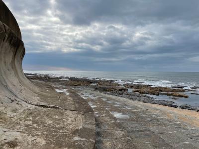Scenic view of a curved sea wall and rocky shoreline under a cloudy sky in Arcozelo, Portugal.