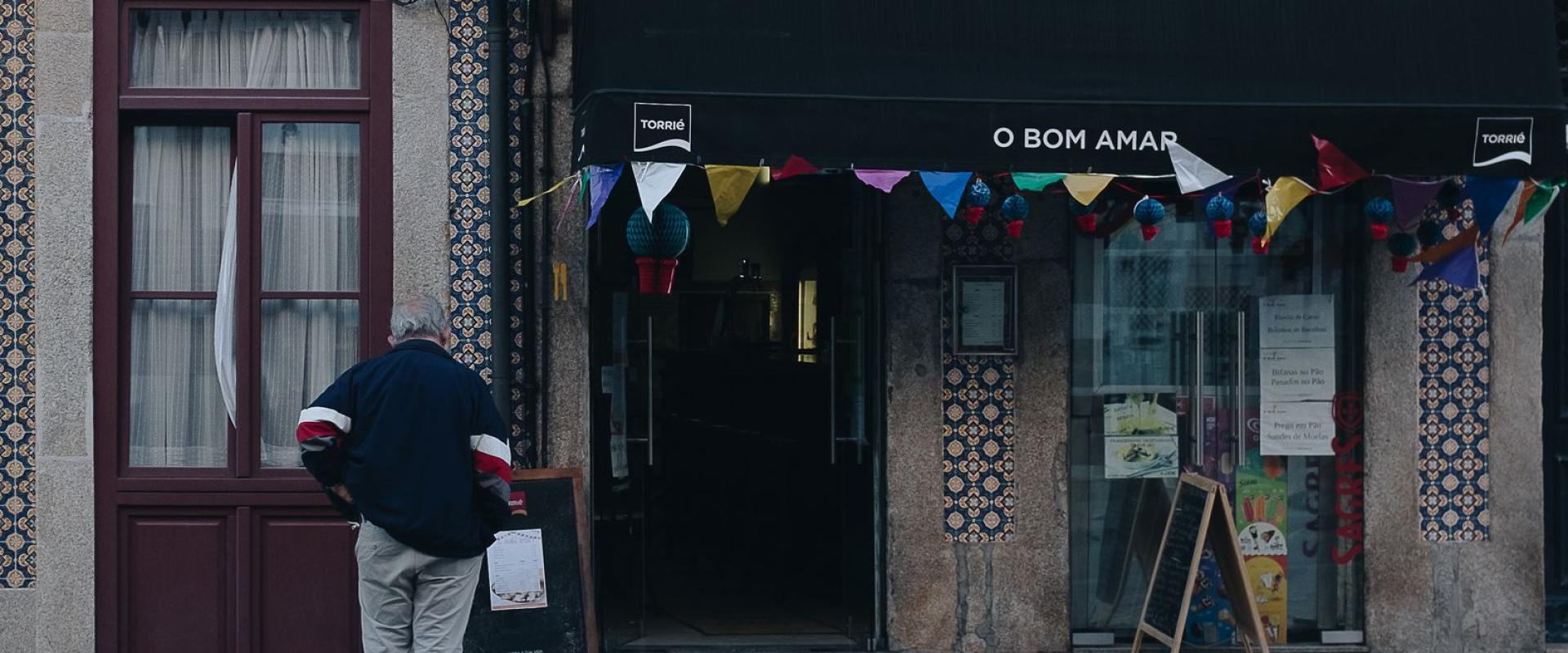 A man stands in front of a decorated Portuguese storefront during the day.