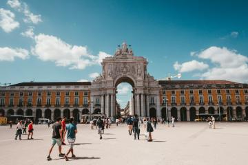 A crowd of tourists walking on a patterned stone street towards a large triumphal arch in a European city square.