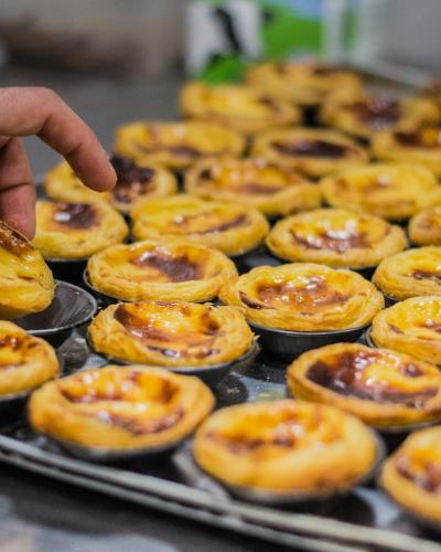 Hand lifting a freshly baked pastel de nata from a tray in Lisbon, Portugal