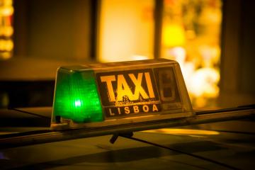 A close-up of a taxi roof light with a green illuminated section and the text "TAXI LISBOA" on a dark background.