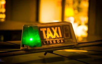 A close-up of a taxi roof light with a green illuminated section and the text "TAXI LISBOA" on a dark background.