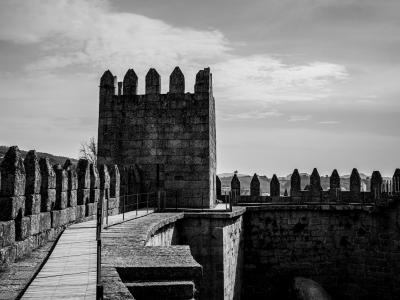 A black-and-white photograph showing the stone battlements and a central tower of a medieval castle, with a paved walkway along the ramparts.