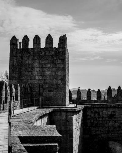 A black-and-white photograph showing the stone battlements and a central tower of a medieval castle, with a paved walkway along the ramparts.