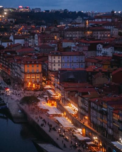 A high-angle view of the Ribeira district in Porto, Portugal, at twilight, showing the Douro River, traditional buildings, and outdoor dining areas along the quay.