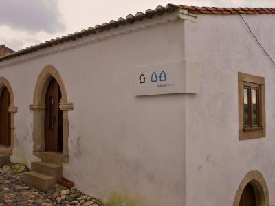 A white-walled building with Gothic-style arched doorways and a cobblestone path, featuring a modern sign that reads "SINAGOGA // MUSEU".