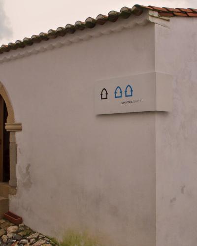 A white-walled building with Gothic-style arched doorways and a cobblestone path, featuring a modern sign that reads "SINAGOGA // MUSEU".