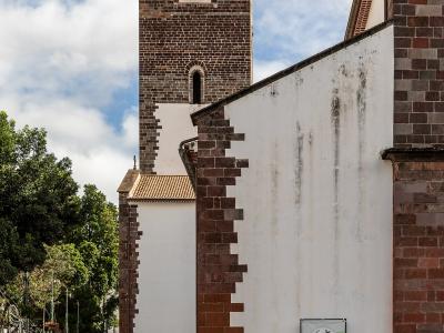 A view of a white-walled church with distinctive reddish-brown stone quoins and a tiled bell tower, featuring a green banner on the wall.