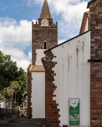 A view of a white-walled church with distinctive reddish-brown stone quoins and a tiled bell tower, featuring a green banner on the wall.