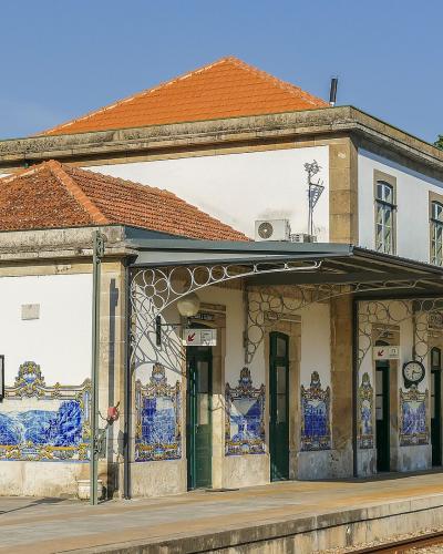 A white railway station building with a terracotta tiled roof, decorated with traditional blue and white azulejo tiles, featuring a platform sign that reads "PINHÃO".