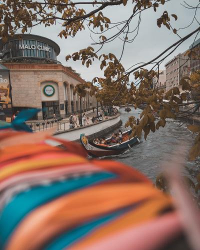 The image shows a Moliceiro boat with passengers navigating a canal, passing a building with a "MAUS CINE" sign, framed by autumn leaves.