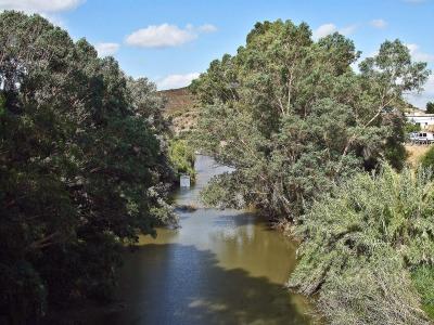 A calm river flowing through a lush, tree-lined valley under a blue sky, with a watermark in the bottom right corner reading "Portuguese_eyes / Vitor Oliveira".