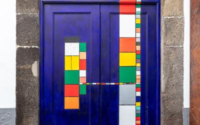 A close-up of a vibrant blue double door with colorful geometric patterns, framed by dark stone, featuring a small plaque reading "S. CASA DA N.º 39" and a sign for "MUNDIAL SAPATARIAS" at the bottom.