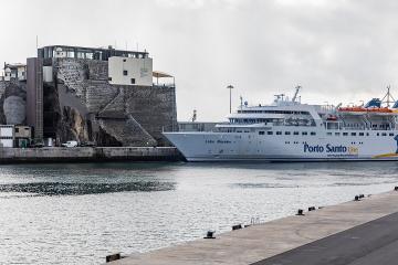 A white passenger ferry named "Lobo Marinho" operated by "Porto Santo Line" is docked at a harbor next to a historic stone fortification built into a rocky cliffside.