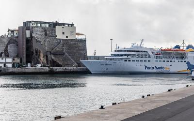 A white passenger ferry named "Lobo Marinho" operated by "Porto Santo Line" is docked at a harbor next to a historic stone fortification built into a rocky cliffside.