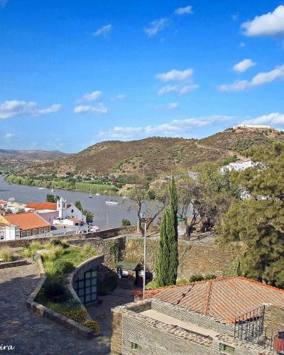 A high-angle view from a stone terrace overlooking the town of Alcoutim, the Guadiana River, and the Alcoutim Castle ruins on a distant hill.