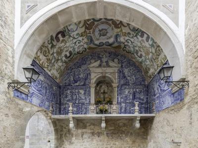 The image shows the interior of a stone archway featuring a small chapel with blue and white azulejo tiles and a painted vaulted ceiling, with a smaller arched passage visible to the left.
