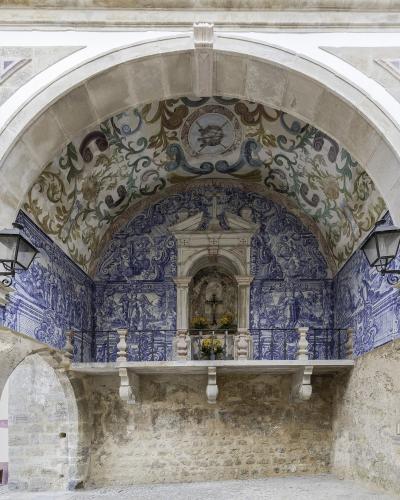 The image shows the interior of a stone archway featuring a small chapel with blue and white azulejo tiles and a painted vaulted ceiling, with a smaller arched passage visible to the left.
