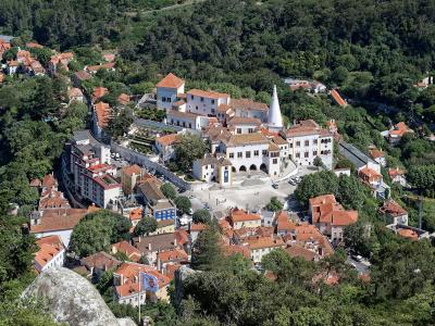 An elevated view of the town of Sintra, Portugal, featuring the National Palace with its distinctive conical chimneys and the surrounding historic buildings and terracotta roofs.