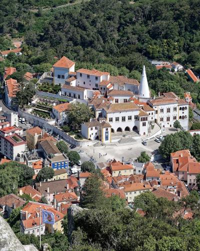 An elevated view of the town of Sintra, Portugal, featuring the National Palace with its distinctive conical chimneys and the surrounding historic buildings and terracotta roofs.