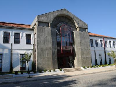 The image shows the exterior of a large building with a central concrete archway and red-framed glass entrance, flanked by white wings with terracotta roofs, featuring the text "Termas de Monção" on the facade.