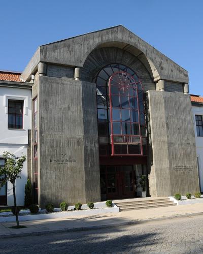 The image shows the exterior of a large building with a central concrete archway and red-framed glass entrance, flanked by white wings with terracotta roofs, featuring the text "Termas de Monção" on the facade.