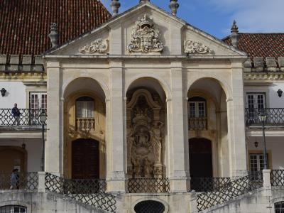 A low-angle photograph of the ornate stone facade of the Chapel of St. John the Baptist (Capela de São João Baptista), featuring three arched doorways, a central sculpted niche, and a coat of arms above the pediment, with a wide staircase leading up 