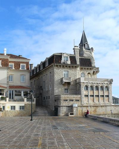 A waterfront promenade in Cascais, Portugal, featuring the stone Palácio dos Condes de Castro Guimarães on the right and the adjacent Palácio de Seixas on the left.