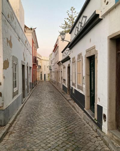 A narrow, cobblestone street lined with traditional white-washed buildings featuring stone window frames and a green door, viewed from a low angle looking uphill.