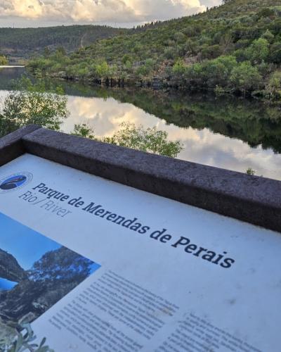 A close-up of an informational sign for "Parque de Merendas de Perais" with a view of a river and forested hills in the background.
