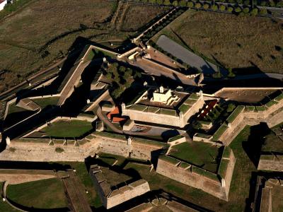 An aerial photograph of a large, star-shaped historic military fortification with stone ramparts, grassy courtyards, and a central building complex, set in a rural landscape with roads and fields.