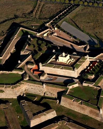 An aerial photograph of a large, star-shaped historic military fortification with stone ramparts, grassy courtyards, and a central building complex, set in a rural landscape with roads and fields.