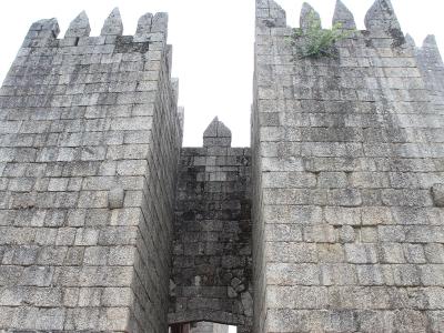 A low-angle view of the stone gatehouse towers and battlements of a medieval castle, showing the entrance passage between two fortified walls.