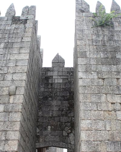 A low-angle view of the stone gatehouse towers and battlements of a medieval castle, showing the entrance passage between two fortified walls.