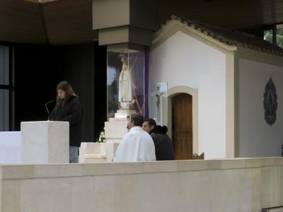 A small, white-walled chapel with a tiled roof and a blue tile mural of Our Lady of Fátima on the exterior wall, situated inside a larger modern building with a congregation seated in the foreground.