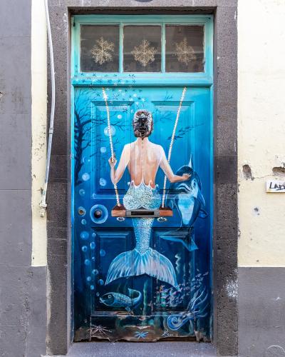 A close-up photograph of a blue wooden door painted with a mermaid on a swing, featuring the house number 105 above the frame.
