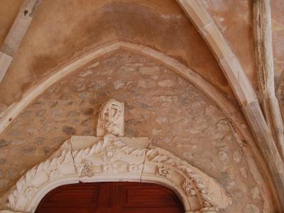 A close-up architectural detail of a stone doorway featuring a pointed Gothic arch, a carved keystone, and an ornate, rope-twist style architrave above a wooden door.