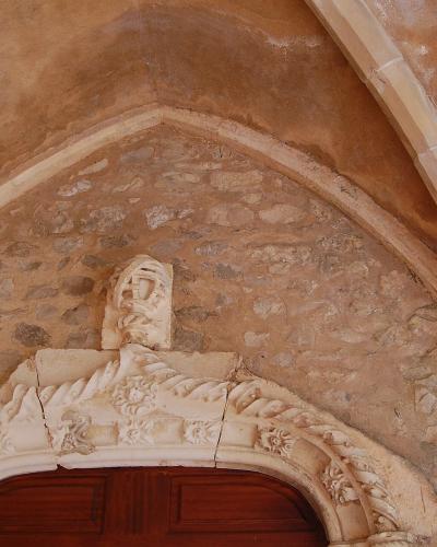 A close-up architectural detail of a stone doorway featuring a pointed Gothic arch, a carved keystone, and an ornate, rope-twist style architrave above a wooden door.