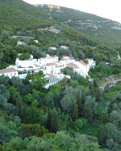 A cluster of white buildings with terracotta roofs nestled into a densely forested hillside, viewed from a distance.