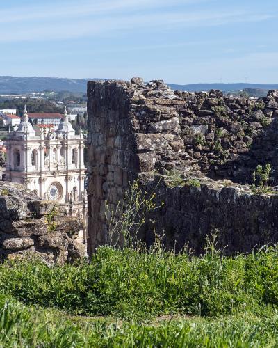 A view through the stone ruins of a medieval fortress looking out towards a large, white Baroque-style church with twin towers in the background.