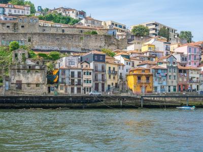 A view from the Douro River looking up at the colorful, terraced buildings of the Ribeira district in Porto, Portugal, with a stone retaining wall and a small boat on the water.