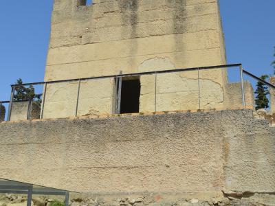 A low-angle shot of a weathered stone tower with crenellations and a modern metal railing, set against a clear blue sky.