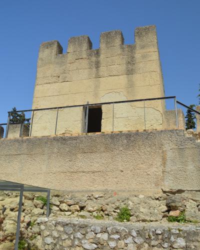 A low-angle shot of a weathered stone tower with crenellations and a modern metal railing, set against a clear blue sky.