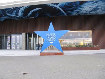 A large blue star sculpture stands in front of a modern building entrance, with text on the star reading "MUSEU FUTEBOl CLUBE DO PORTO" and a mural of a dragon above.