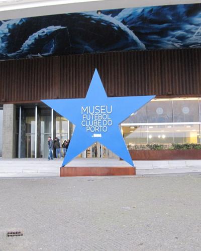 A large blue star sculpture stands in front of a modern building entrance, with text on the star reading "MUSEU FUTEBOl CLUBE DO PORTO" and a mural of a dragon above.