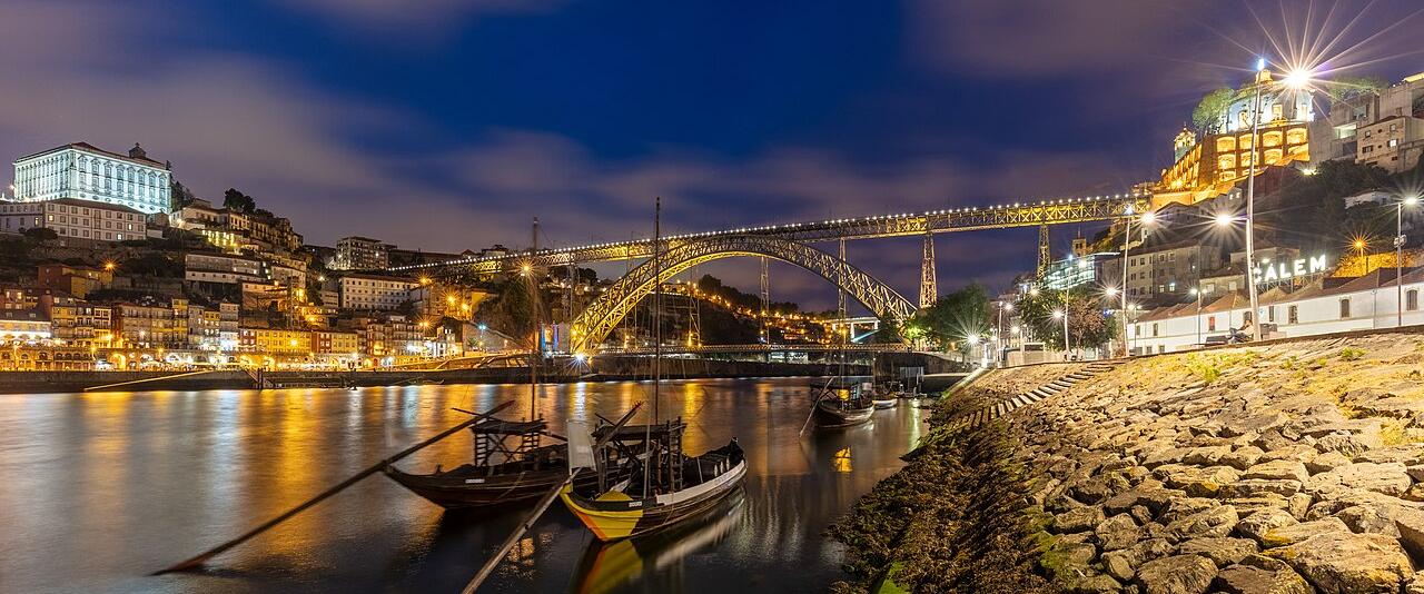 The Dom Luís I Bridge and the Ribeira at dusk, with rabelo boats on the Douro